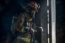 Firefighter walking out of door into sunlight with smoke coming off him