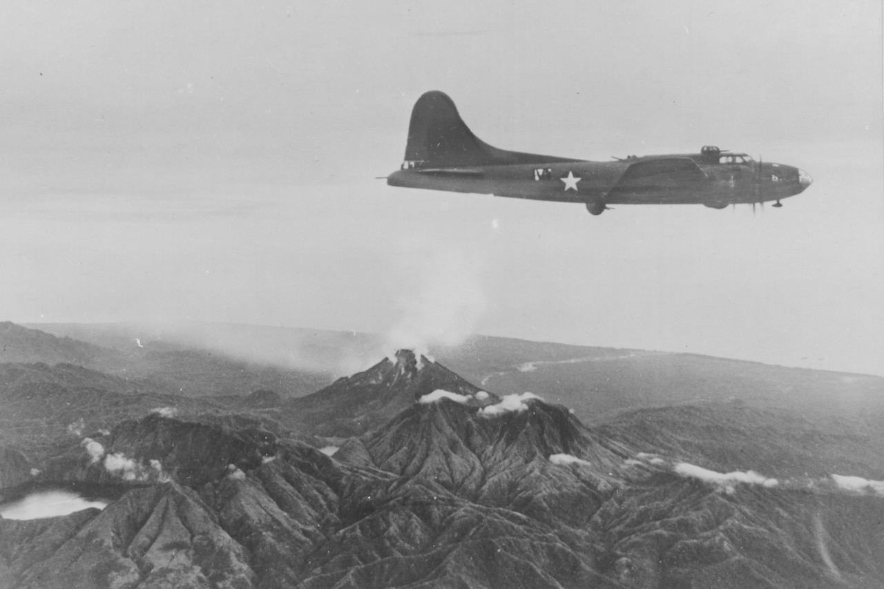 An airplane flies over land that includes an active volcano and a crater lake.