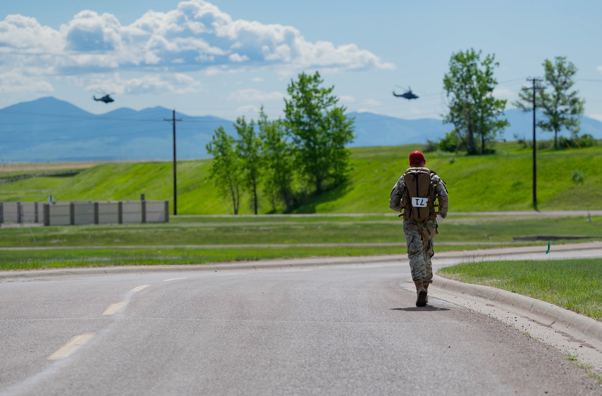 Airman with ruck sack running with two helicopters in the background.
