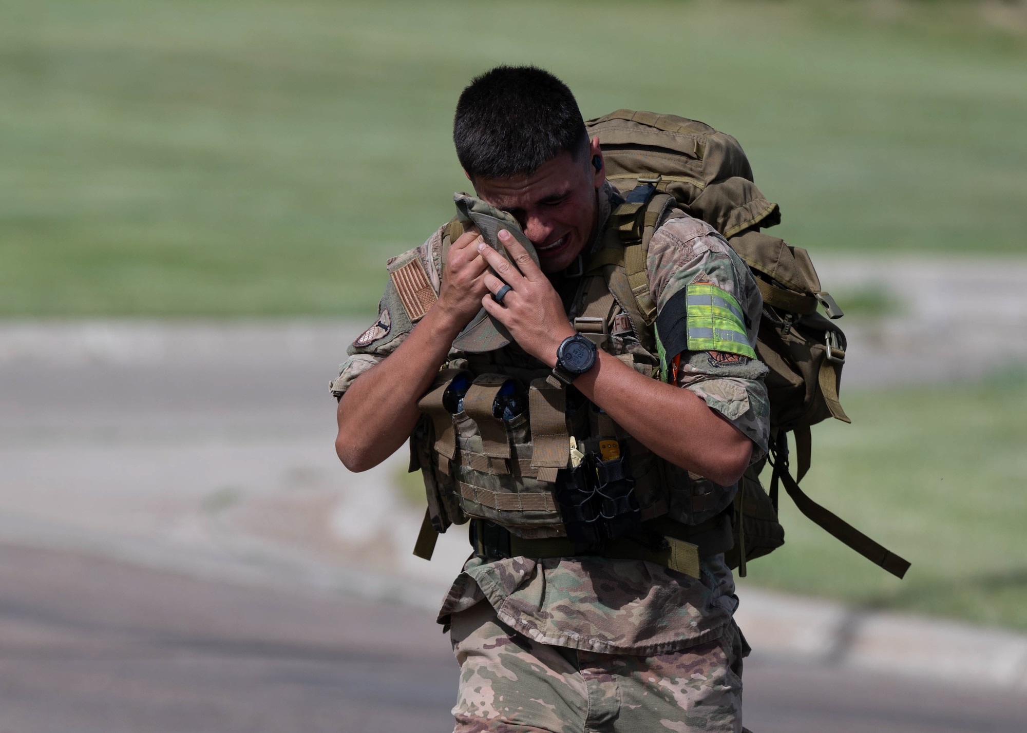 Airman carrying ruck sack wiping sweat.
