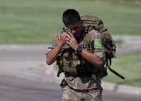 Airman carrying ruck sack wiping sweat.