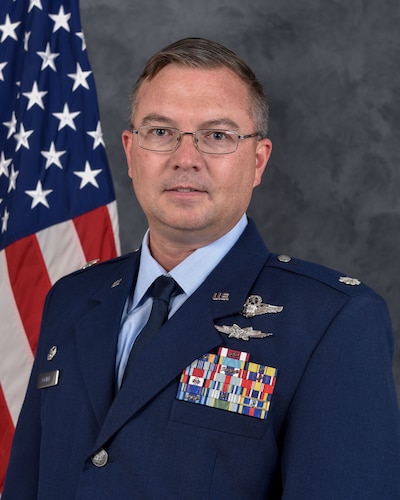 photo of a uniformed US Airman standing in front of a US flag