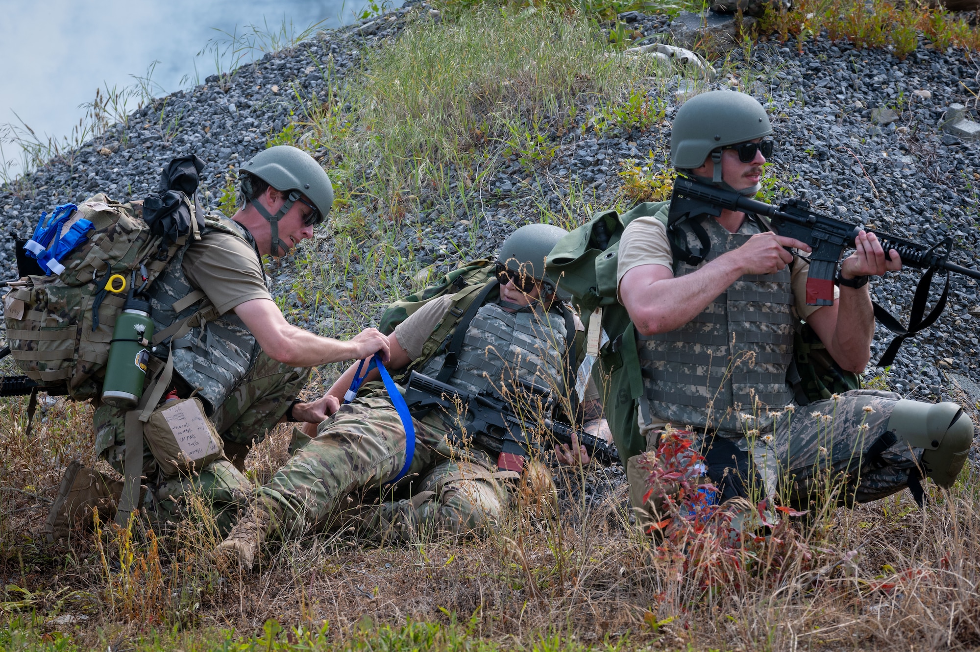 one person aims a weapon while another renders aid to a simulated casualty