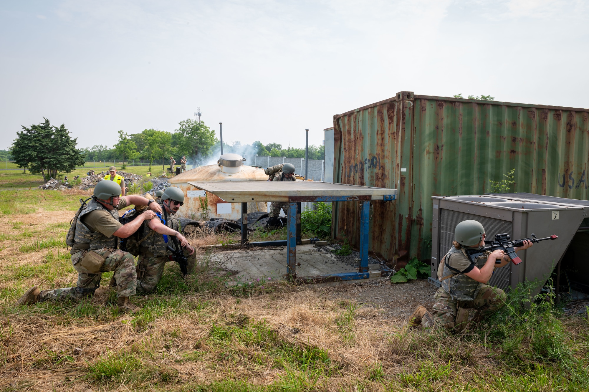 one person is kneeling with a weapon, another on assists a simulated casualty