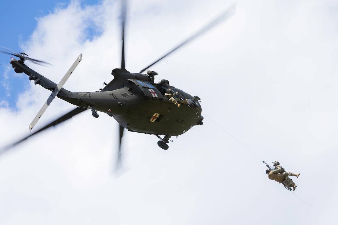 Two soldiers attached to a line are hoisted toward a flying helicopter as another soldier at an open door of the aircraft holds the line.