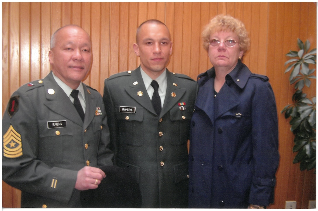Two men wearing military uniforms stand next to a woman in a posed photo.
