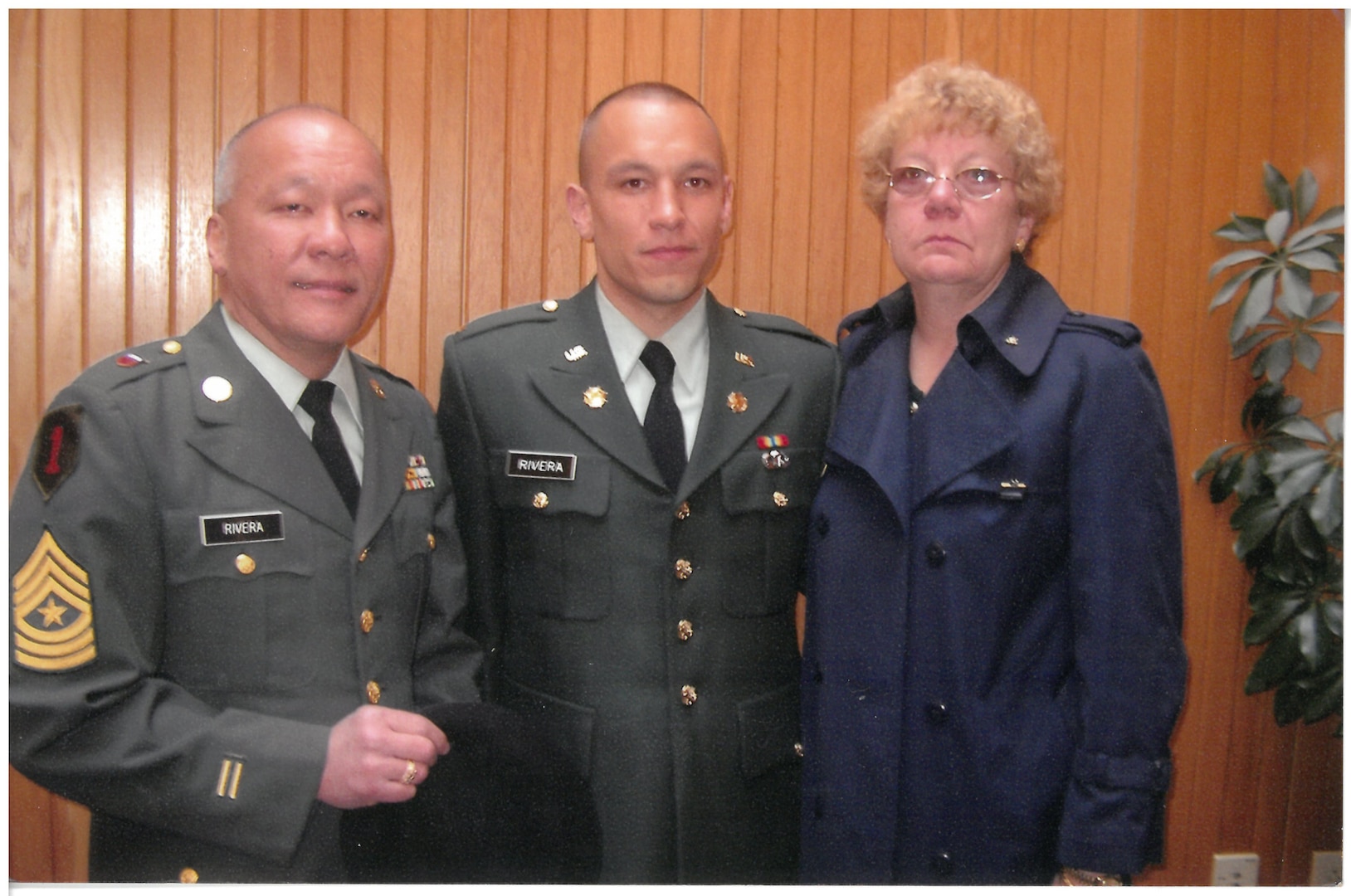 Two men wearing military uniforms stand next to a woman in a posed photo.