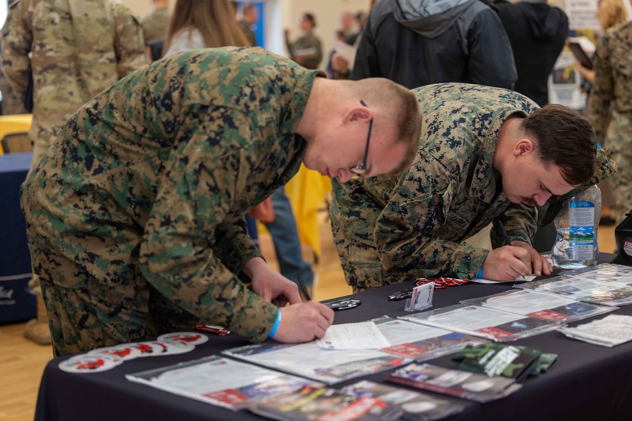 Two Marines lean over a table and write on documents.