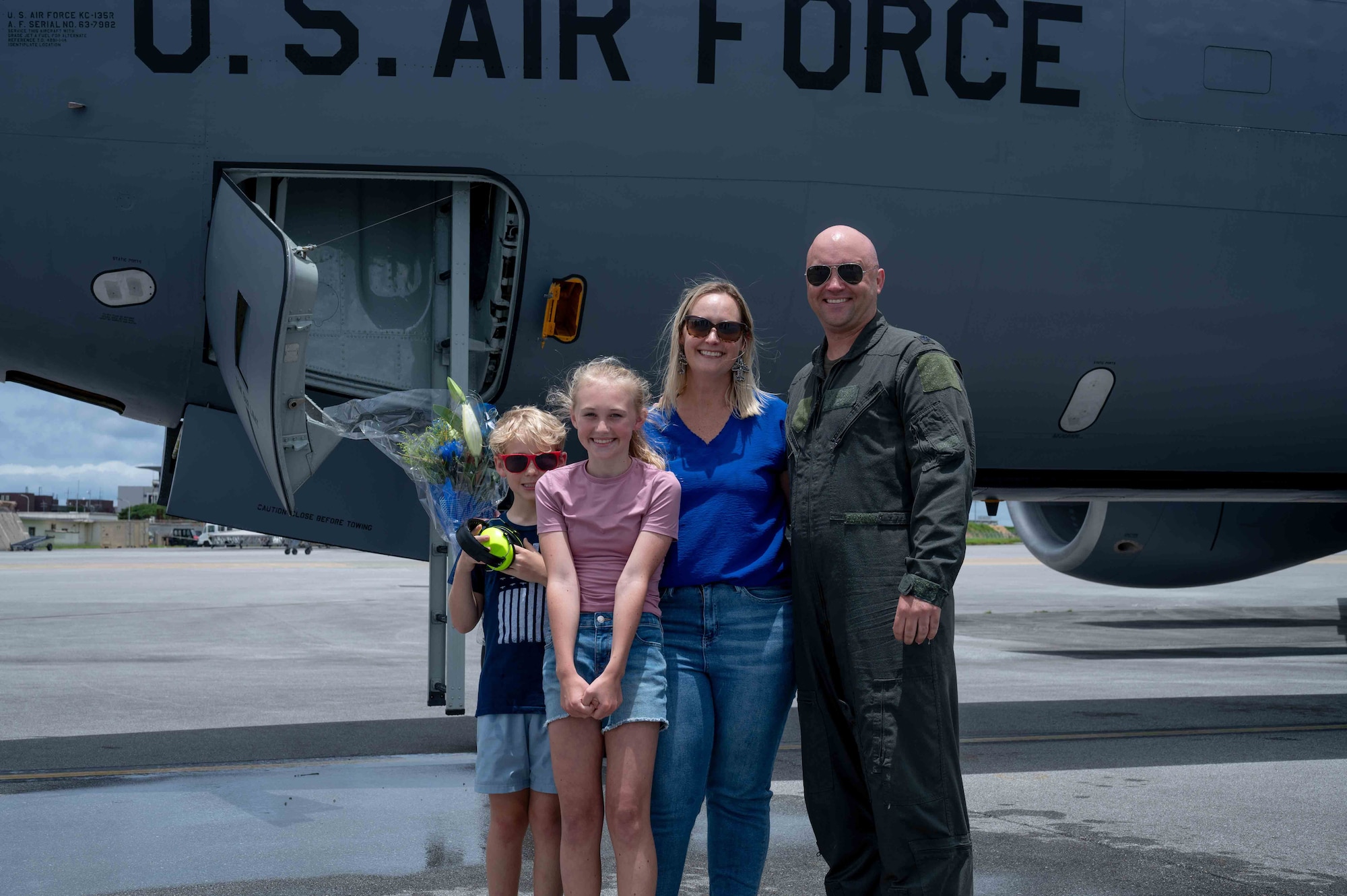 military member and his family stands with arms crossed Infront of an aircraft