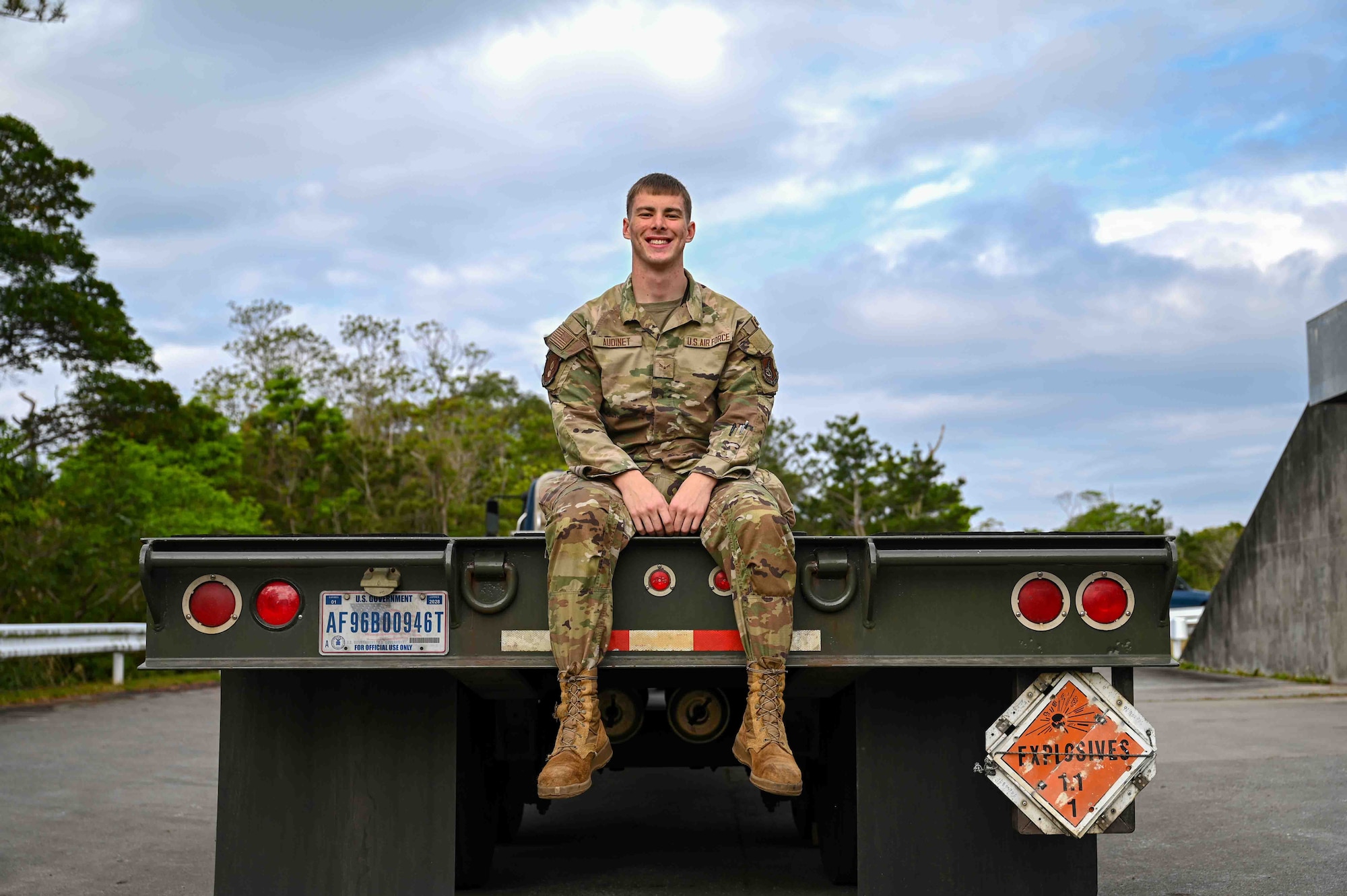 A U.S. Air Force Airman poses for a photo while sitting on the bed of a truck.