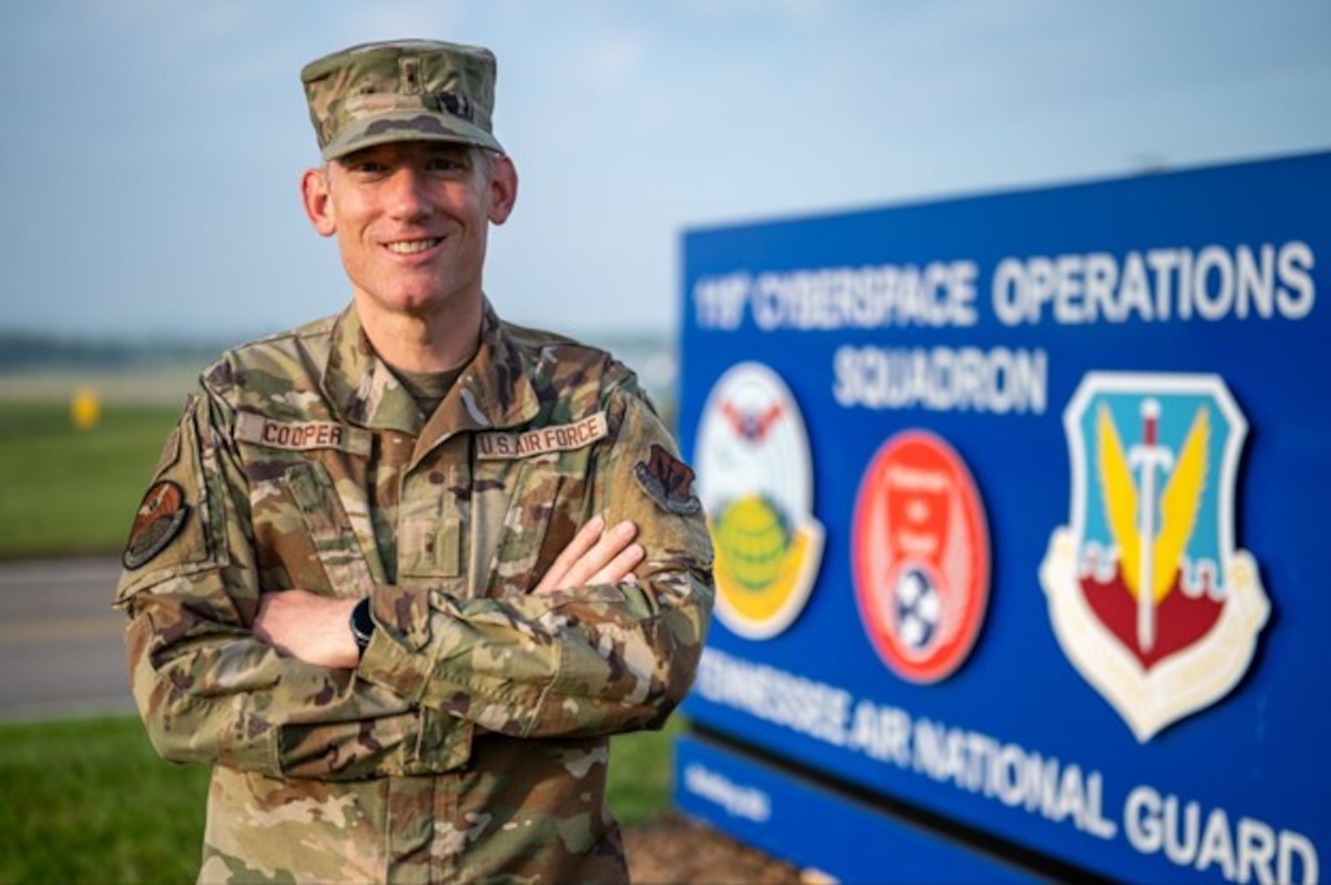 Warrant Officer 1 Curtis Cooper stands in front of the 119th Cyber Operations Squadron sign.