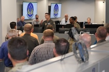 photo of a large room with people standing listening to a US Airman speak