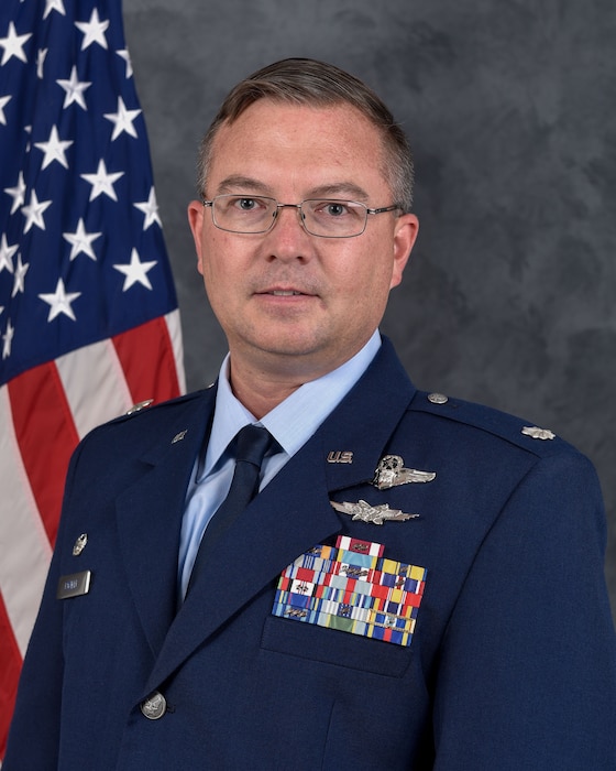 photo of a uniformed US Airman standing in front of a US flag