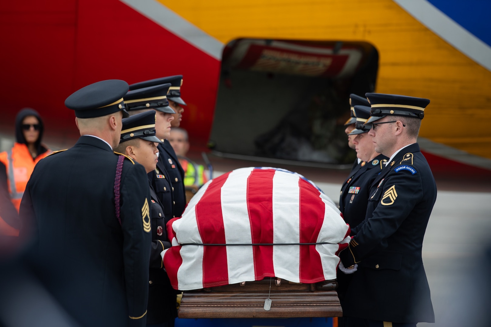 Military personnel remove casket from aircraft and transfer it to a hearse