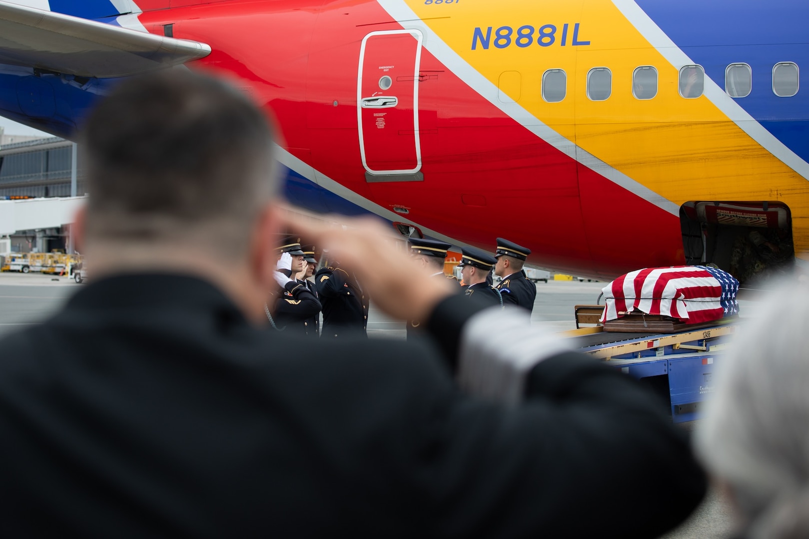 Military personnel remove casket from aircraft and transfer it to a hearse