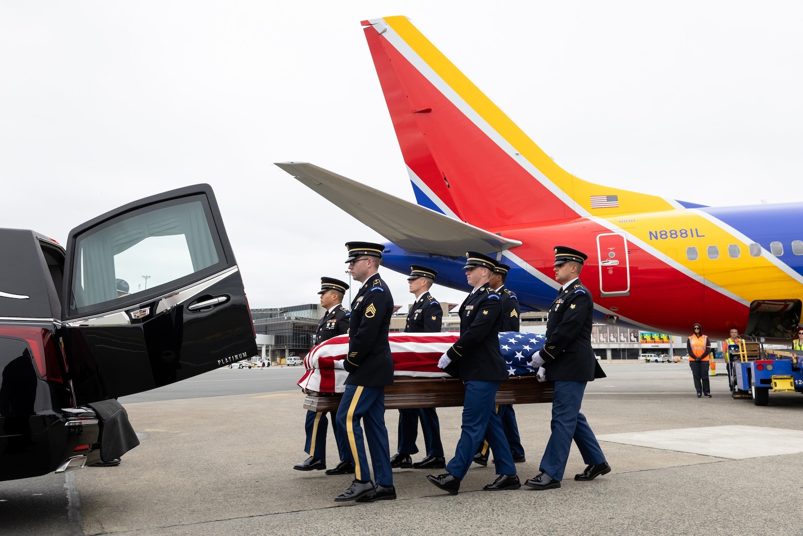 Military personnel remove casket from aircraft and transfer it to a hearse