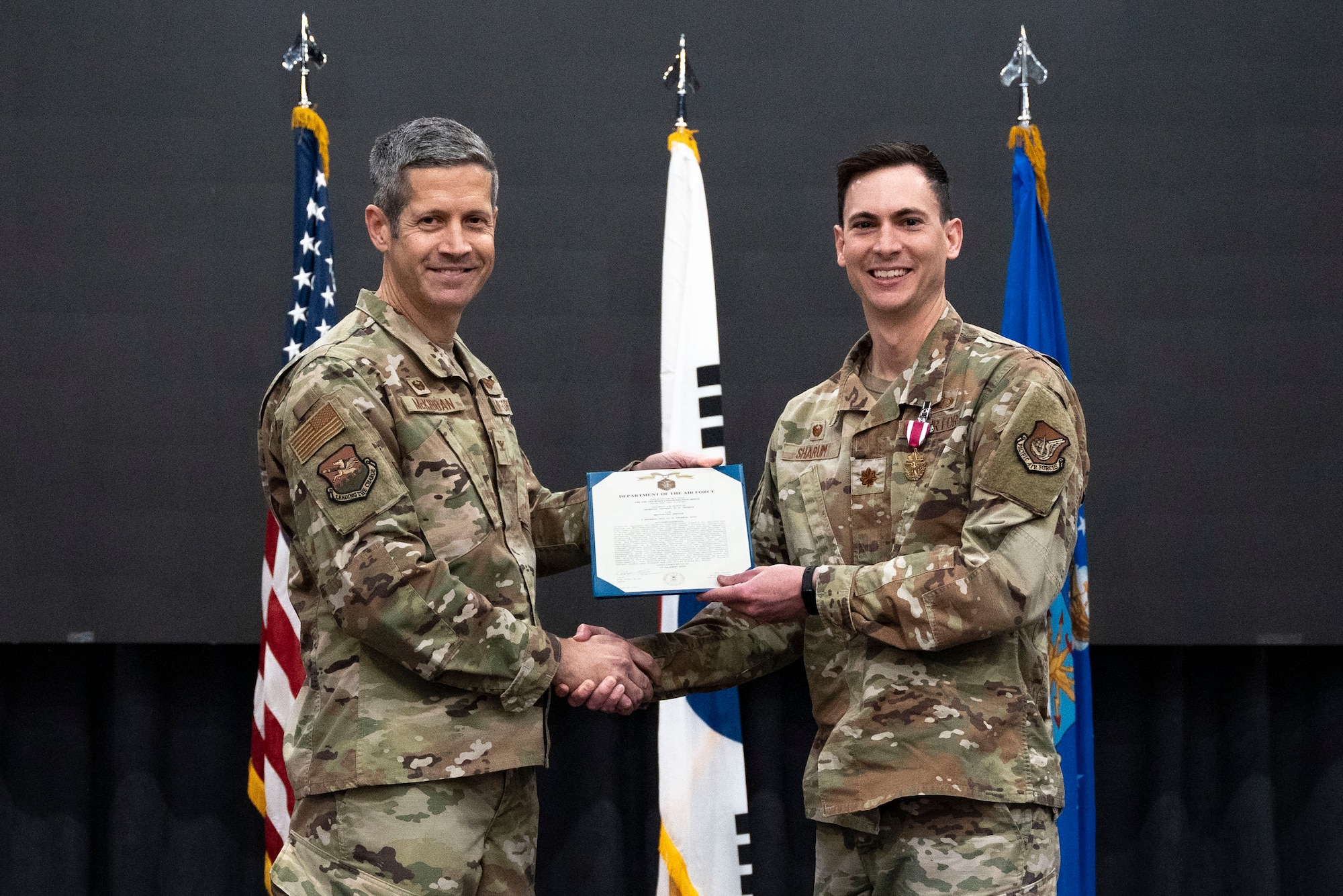 U.S. Air Force Maj. Clayton Sharum, right, outgoing 51st Comptroller Squadron commander, right, receives the Meritorious Service Medal from Col. William McKibban, left, 51st Fighter Wing commander, during a Change of Command ceremony at Osan Air Base, Republic of Korea, June 13, 2025.