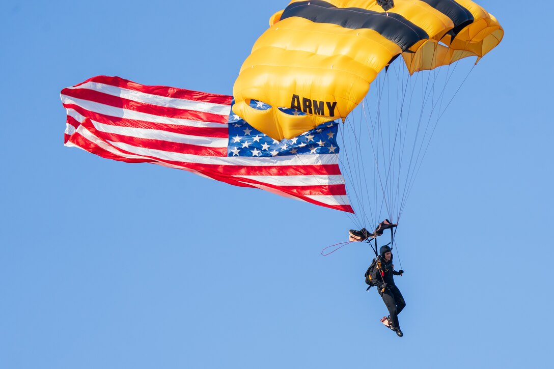 Golden Knights parachuter descends with U.S. flag during an Army 250 celebration.