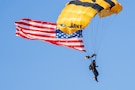 Golden Knights parachuter descends with U.S. flag during an Army 250 celebration.