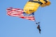 Golden Knights parachuter descends with U.S. flag during an Army 250 celebration.