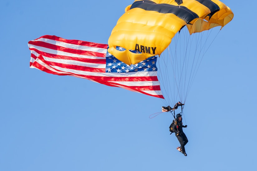 Golden Knights parachuter descends with U.S. flag during an Army 250 celebration.