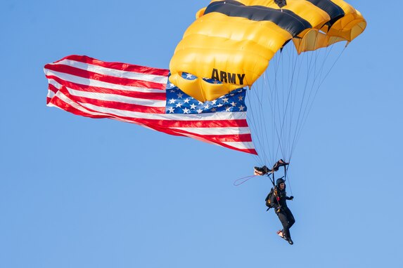 Golden Knights parachuter descends with U.S. flag during an Army 250 celebration.