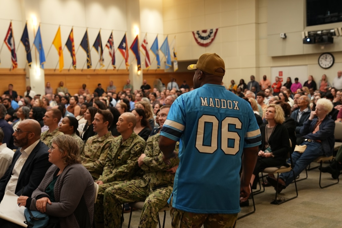 Man in football jersey speaks to an audience.