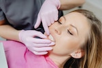 Woman in dental chair, gums being examined by dentist wearing pink gloves