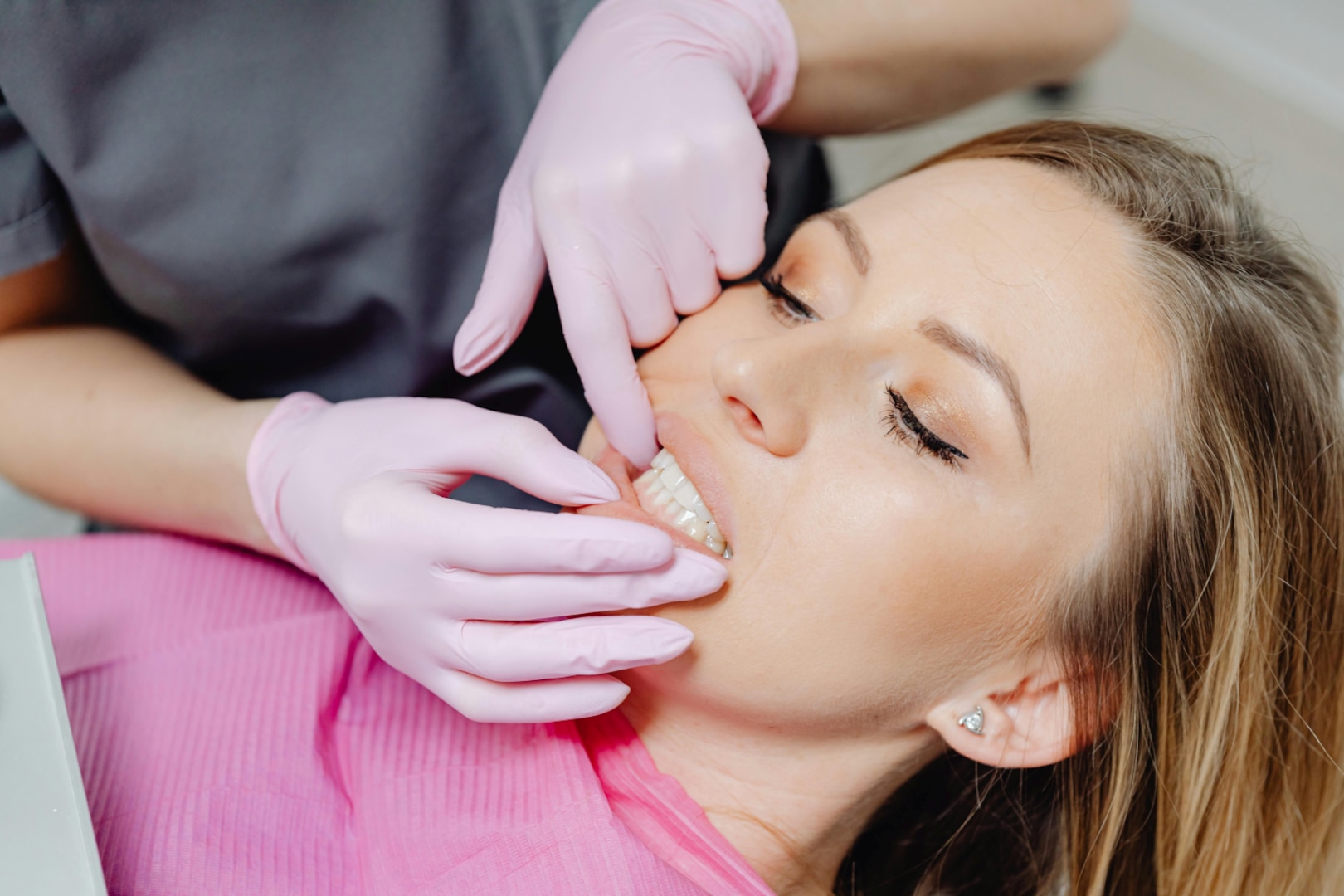Woman in dental chair, gums being examined by dentist wearing pink gloves