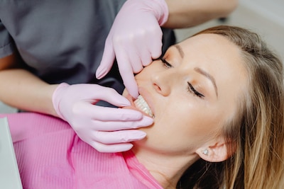 Woman in dental chair, gums being examined by dentist wearing pink gloves