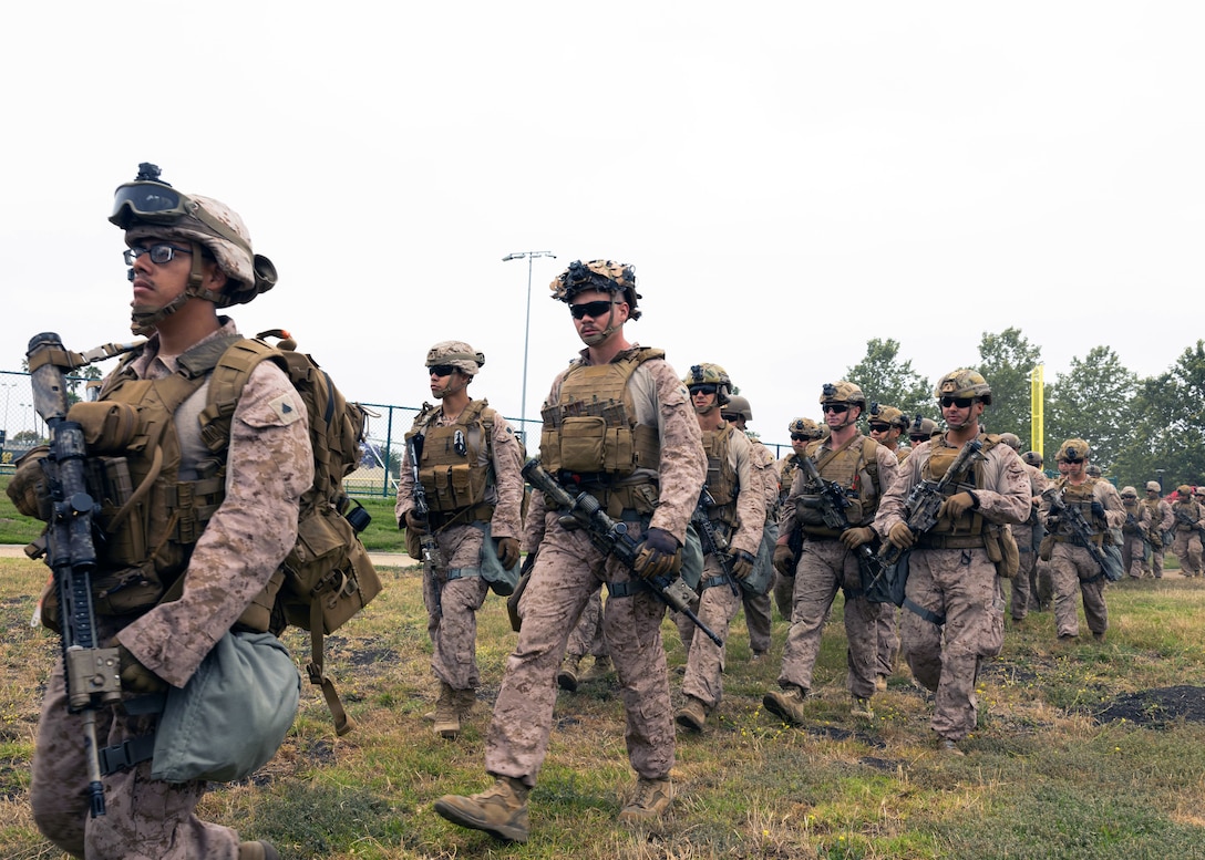 Marines in combat gear casually walk on a grassy field on an overcast day.