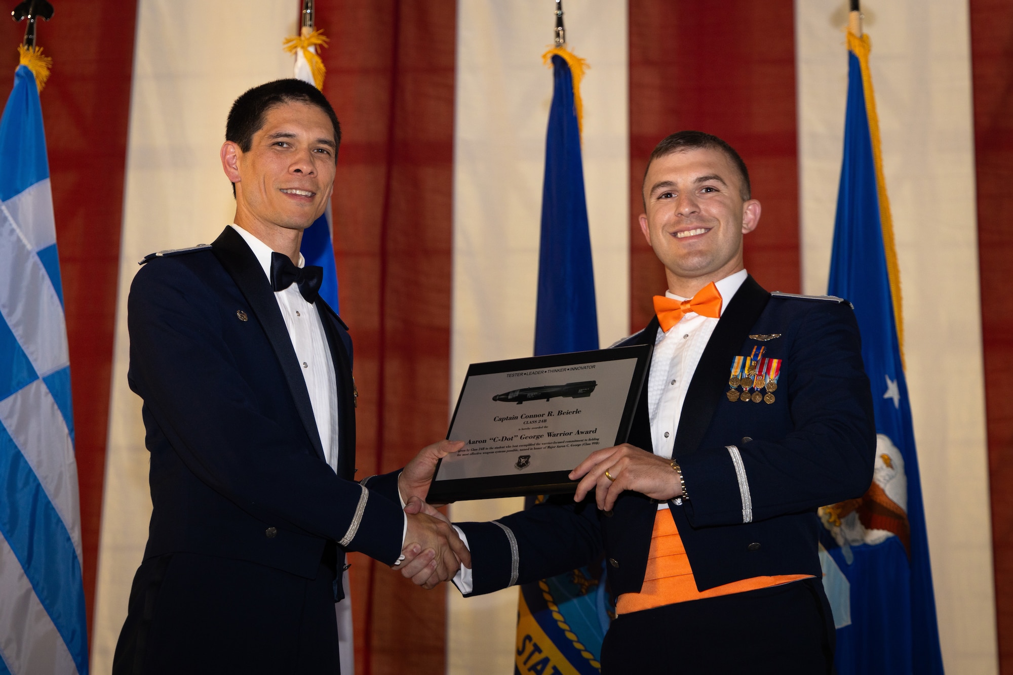 Class 24-Bravo student, Capt. Connor Beierle, receives the Aaron “C-Dot” George Warrior Award from Col. James Valpiani, commandant, Air Force Test Pilot School, at Edwards Air Force Base, CA. The award recognizes a single student each class who exemplifies the warrior-focused commitment to fielding the most effective weapon system. (Air Force Photo by Brandon Hernandez)