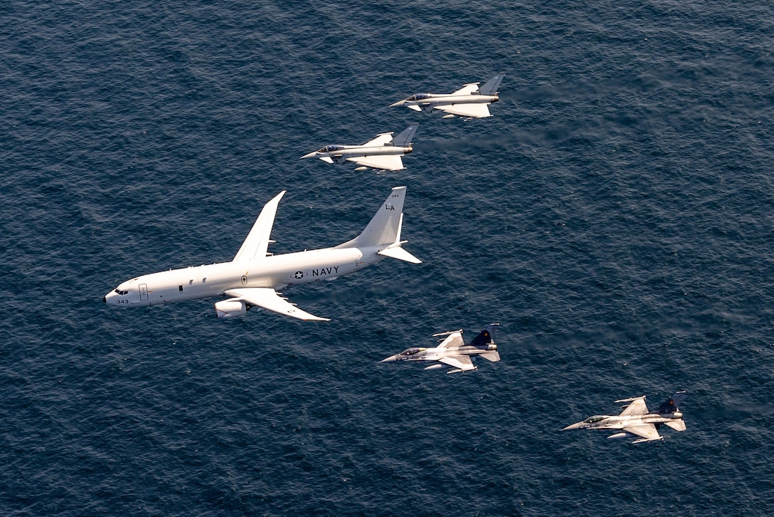 Five aircraft fly in a triangular formation over dark blue water.