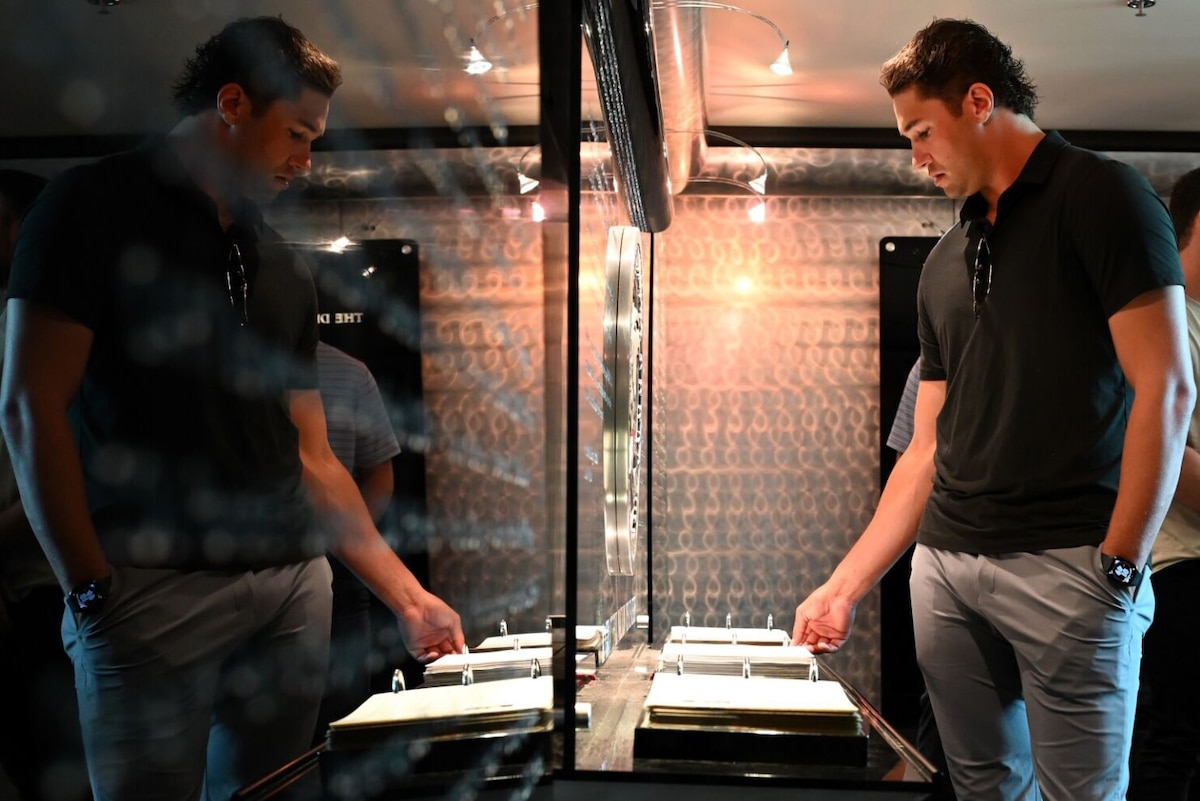 A man wearing casual attire turns a page in a guest book at a memorial wall.