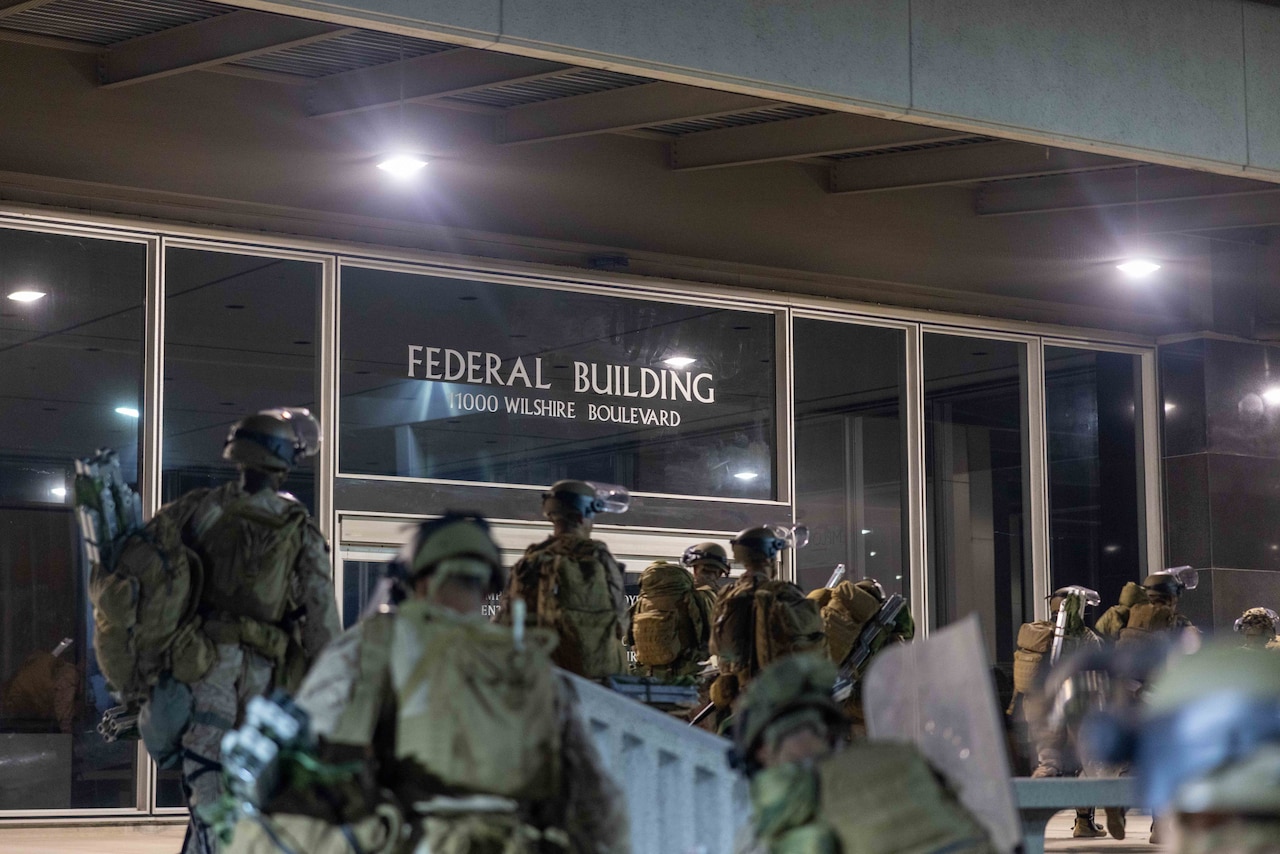 Uniformed service members approach a building with a sign that reads "Federal Building 1000 Wilshire Boulevard."