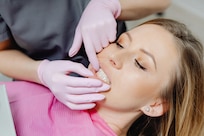 Woman in dental chair, gums being examined by dentist wearing pink gloves