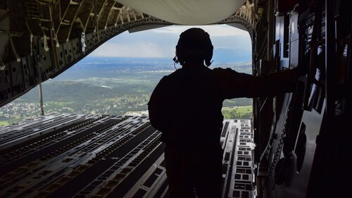 A U.S. Air Force loadmaster views the ground from the cargo bay of a C-17