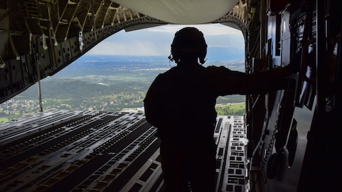A U.S. Air Force loadmaster views the ground from the cargo bay of a C-17