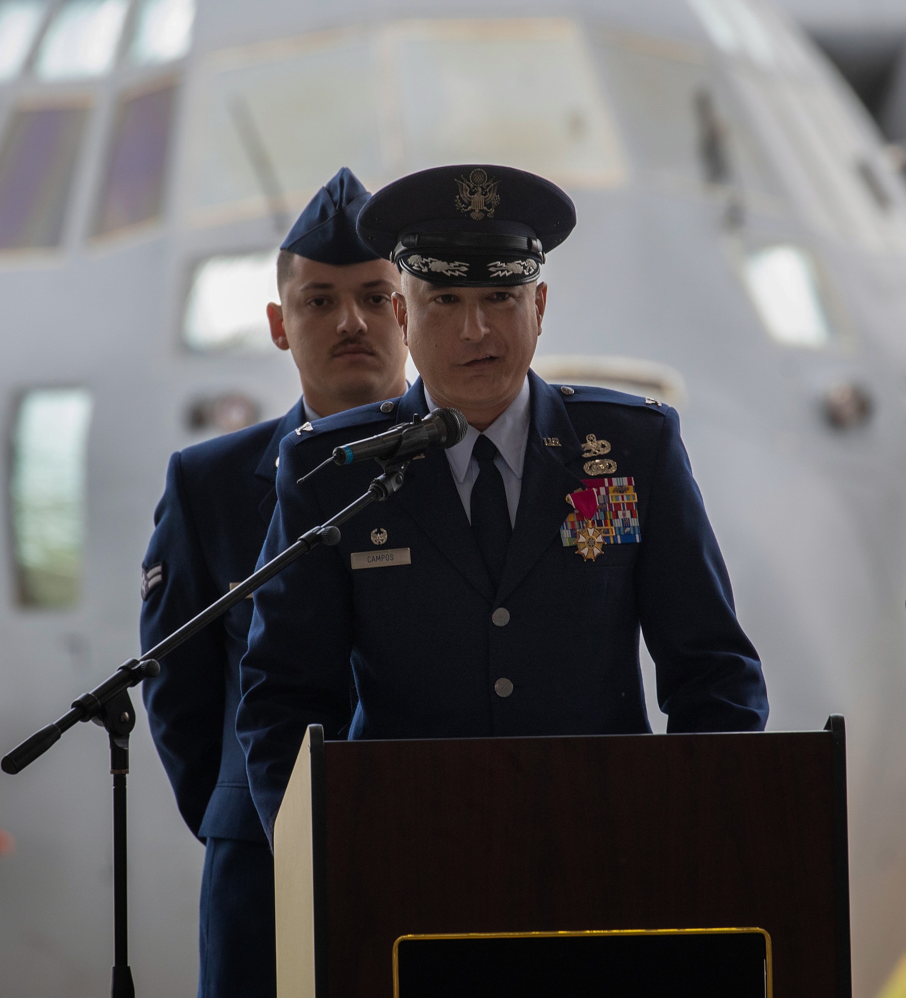 The outgoing 374th MXG commander, dressed in their blue dress uniform, gives remarks during the change of command ceremony in a hangar.