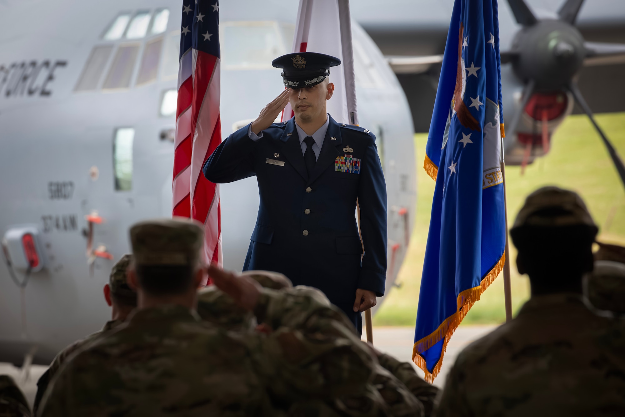 The incoming 374th Maintenance Group commander, dressed in their blue dress uniform, salutes a formation of MXG Airmen inside of a hangar.
