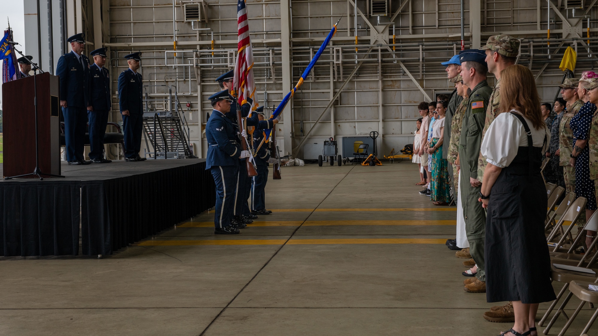 Attendees stand as the honor guard presents the colors inside of a hangar.
