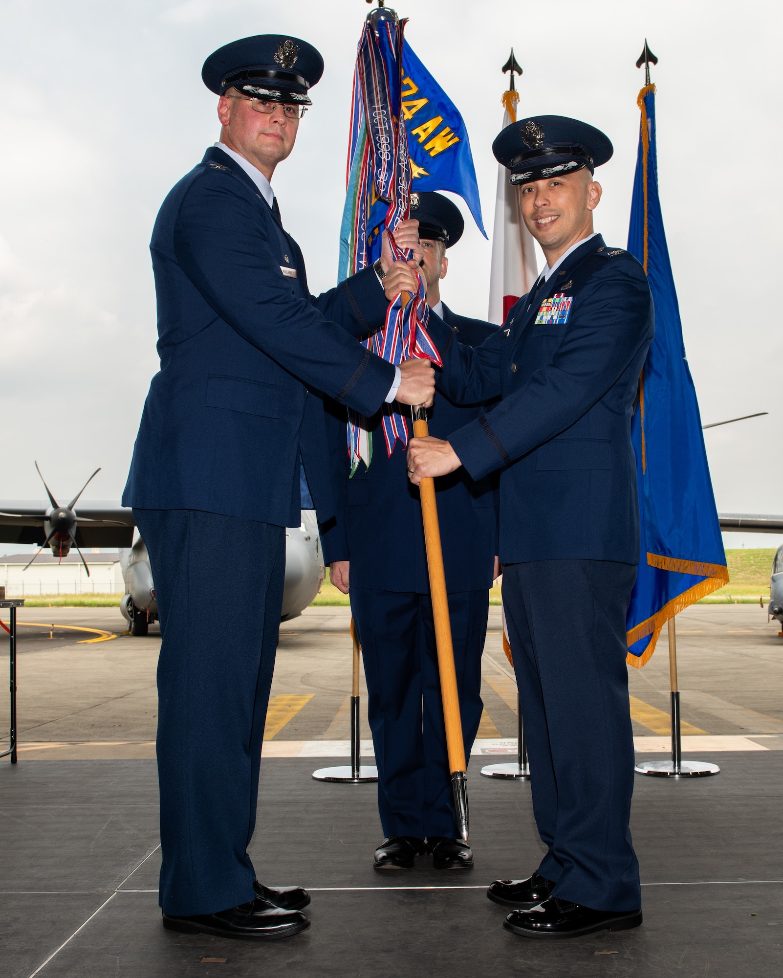U.S. Air Force members dressed in their blue dress uniforms hold a baton with colors and a blue flag at the top.