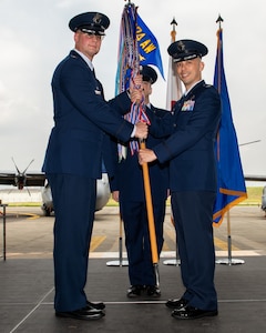 U.S. Air Force members dressed in their blue dress uniforms hold a baton with colors and a blue flag at the top.