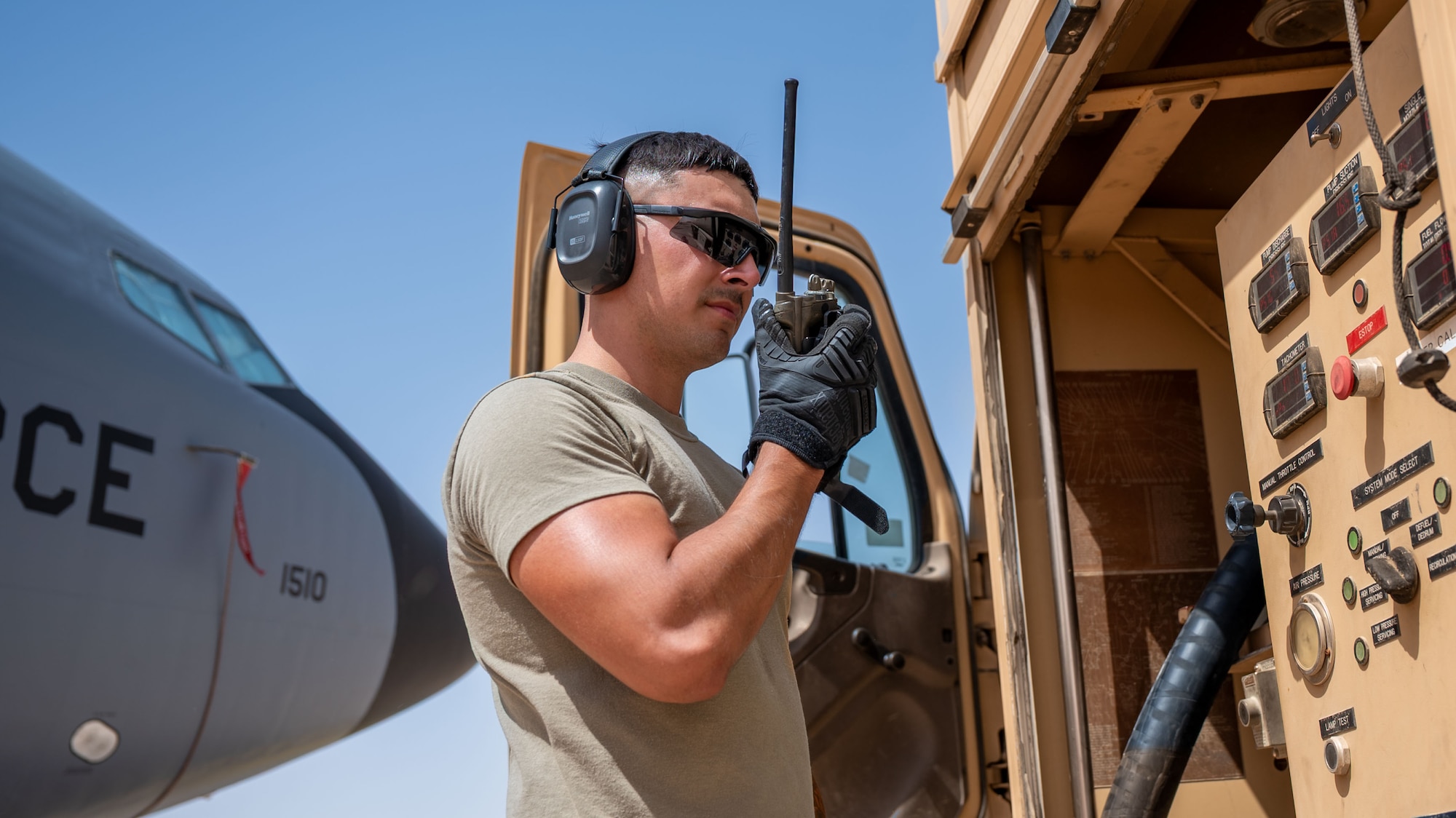 A man uses a handheld radio by a fuel truck.