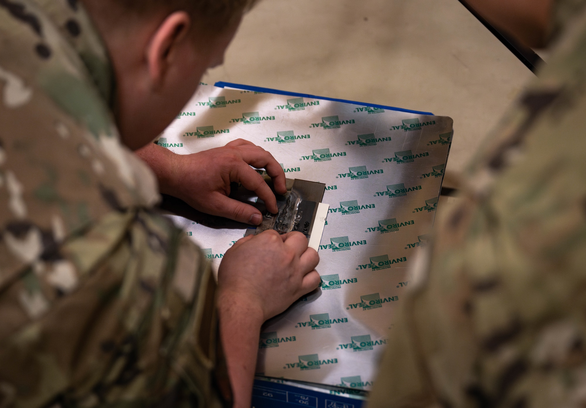 U.S. Air Force Senior Airman Colton Behm, left, and Airman 1st Class Marcus Garrido, 100th Maintenance Squadron non-destructive inspection journeymen, rest a piece of stainless steel sheet metal onto the image plate of a computed radiography during a Day in the Life immersion with the 100th MXS at RAF Mildenhall, England, June 13, 2025.