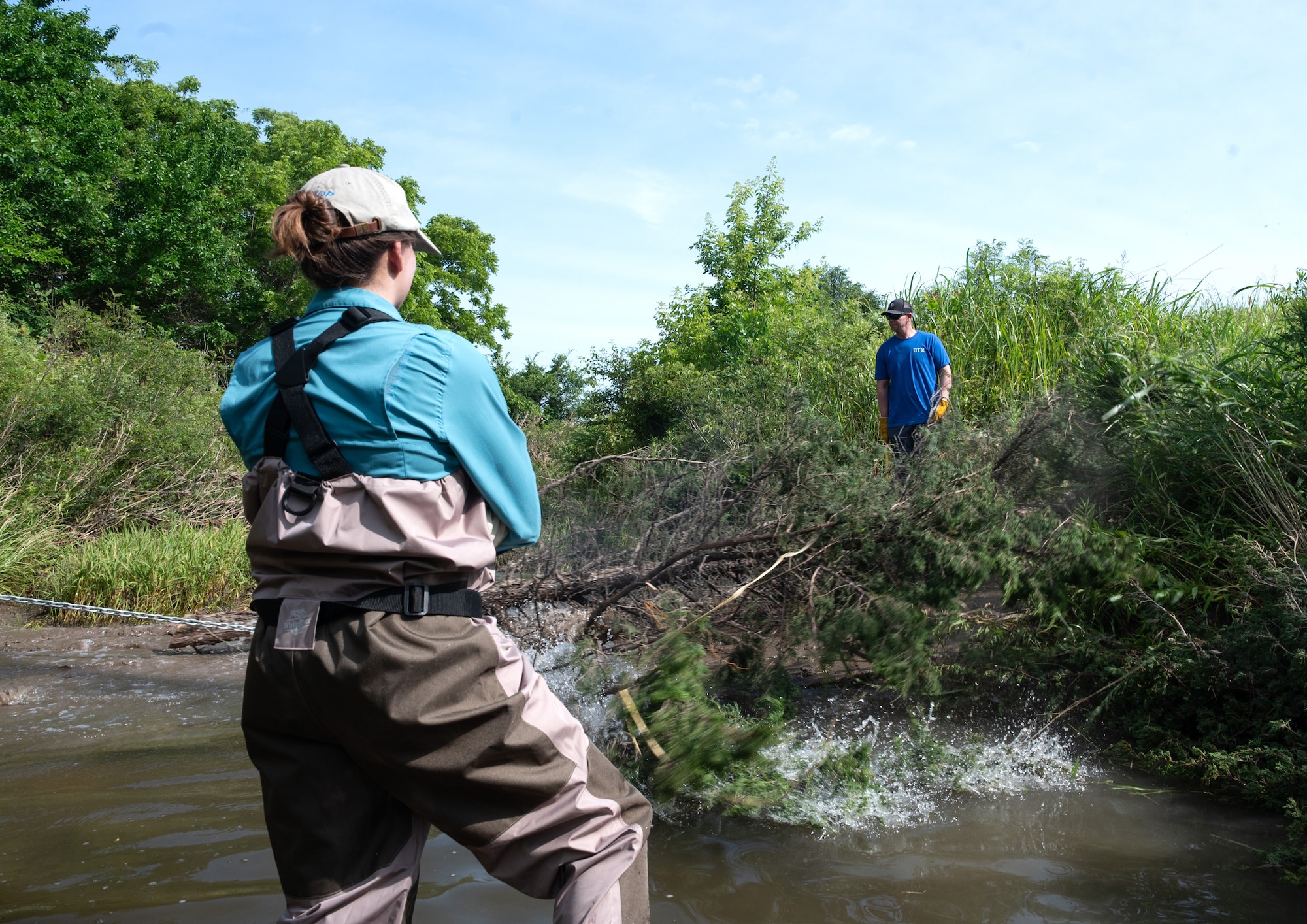 Melina Takvorian, Center for Environmental Management of Military Lands natural resources technician, stands in a creek as a red cedar is dragged into the water during a bank revetment project June 11, 2025, at McConnell Air Force Base, Kansas. Red cedars are invasive to Kansas, so Takvorian, alongside the U.S. Fish and Wildlife Service and 22nd Civil Engineer Squadron, used them for the project as a way to remove invasive flora and fight against erosion. (U.S. Air Force photo by Staff Sgt. Tryphena Mayhugh)