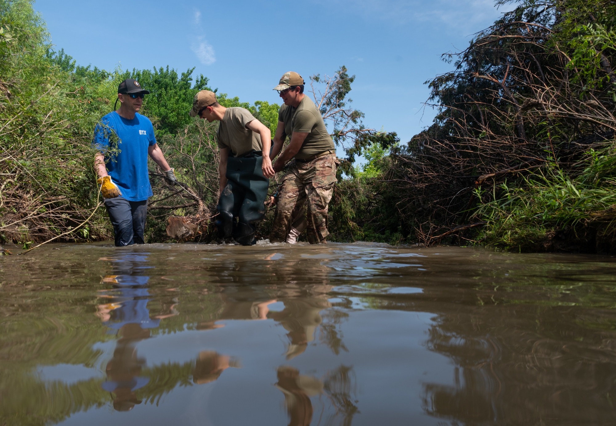 From left, Adam Moore, 22nd Civil Engineer Squadron biologist, and Senior Airman Skylar Ackley and Senior Airman Thomas Roque, 22nd CES explosive ordnance disposal technicians, drag a red cedar through a creek during a bank revetment project June 11, 2025, at McConnell Air Force Base, Kansas. The project used the red cedars to trap dirt and sediment that would allow plant life to grow, stabilizing the bank and preventing erosion. (U.S. Air Force photo by Staff Sgt. Tryphena Mayhugh)
