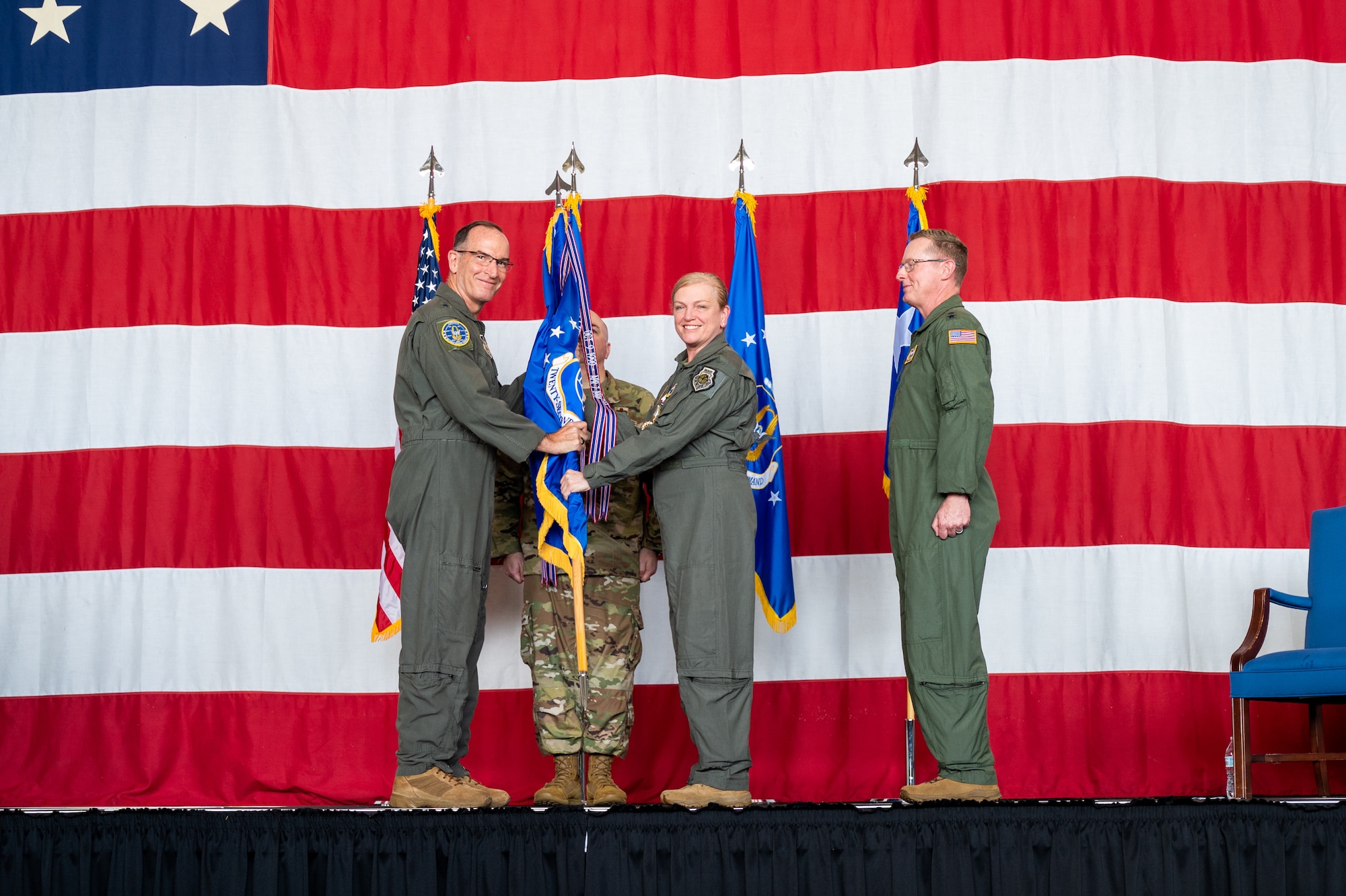 a man and woman in military uniforms hold a guidon while standing on stage in front of flags