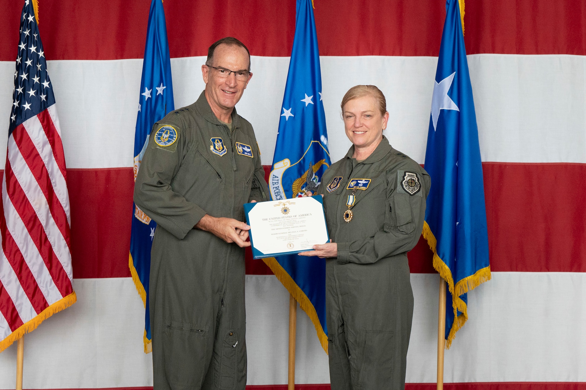 a man and woman in military uniforms stand on stage in front of flags while holding a certificate