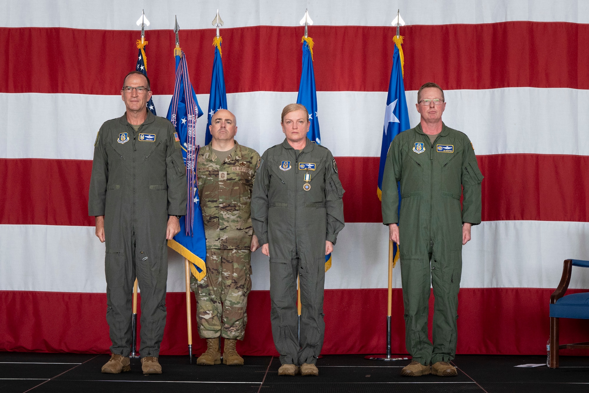 four people in military uniforms stand on stage in front of flags